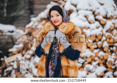 beautiful woman in a fur coat and scarf with firewood. Russian village. Winter.