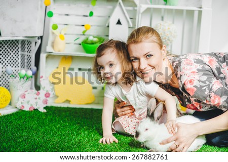 cute baby girl and mother on the grass with white rabbit , smiling, easter decor