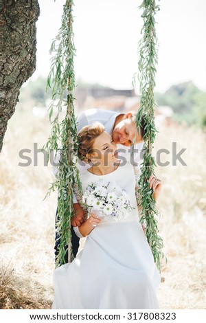 beautiful gorgeous blonde bride and stylish groom on the decorated swing on the tree