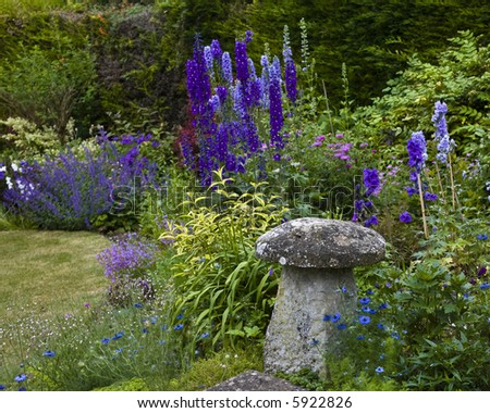 old cottage garden with delphinium and stone mushroom shaped garden ornaments