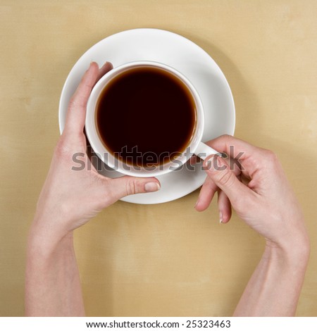 coffee - top view of female hands holding a cup of coffee on a light wood table