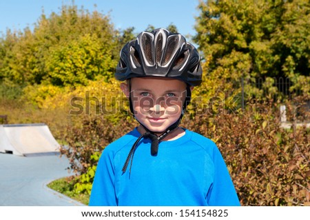 Pretty boy in a bike helmet on the background skate of the park and trees photo taken in the summer.