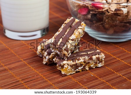bar of chocolate muesli with petals poured with raisins with chocolate in the background milk in the dark key