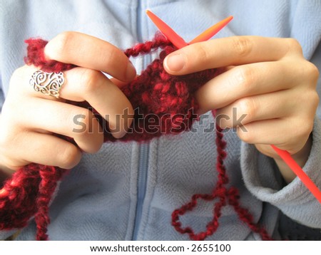 Hands knitting a red scarf on blue background