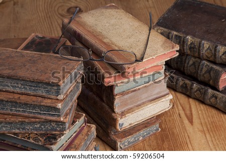 Vintage books are stacked with a pair of reading glasses on top.