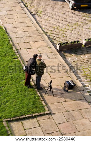 Two people checking shots on a digital camera, tripod and camera bag on the ground.