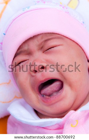 Asian new born in pink dress crying on bed