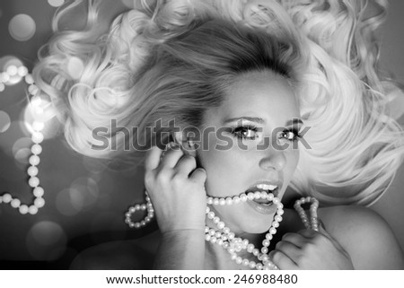 Young beautiful woman with blond curly hair holding pearls in her hand