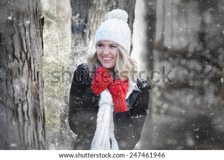 Pretty young woman wearing a coat, scarf and red mittens outdoors in the snow