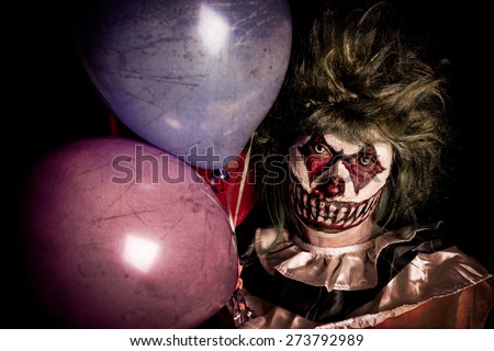 Scary Clown holding balloons in dark shadows