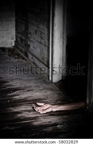 Horror scene of a dead like arm on the floor hanging out of a doorway.