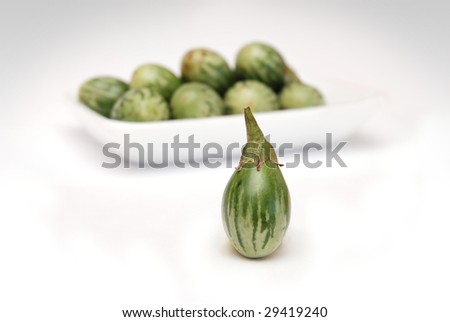 Thai green eggplant fruits on a tray, focus on the one in the foreground, white background.