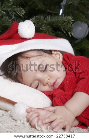 cute baby with santa hat sleeping under christmas tree