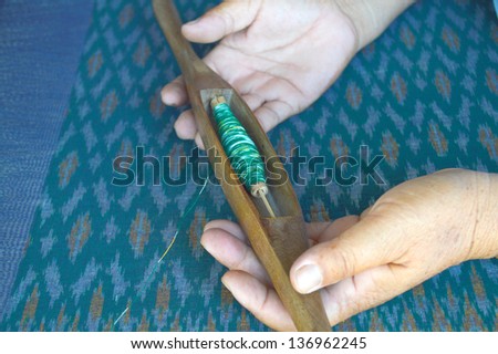 Wooden bobbin in human hands in traditional clothes weaving