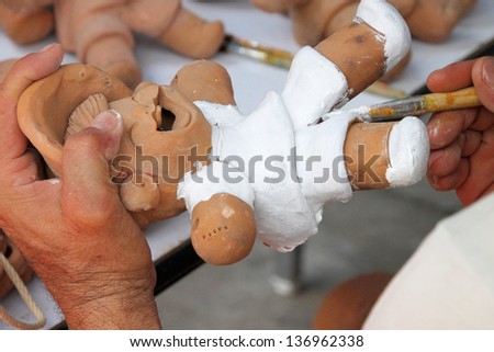 hands of potter, painting an earthen doll white color