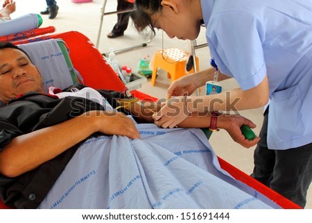 MAHASARAKHAM, THAILAND - AUGUST 21 : Unidentified nurse is stabbing needle in man\'s arm for blood donation at Padung Nari school on August 21, 2013 in Mahasarakham, Thailand.