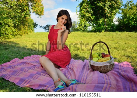 Beautiful girl in a pink dress on a picnic with a basket of fruit