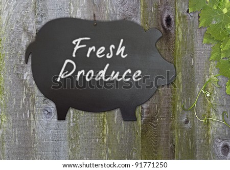 Black Pig Shaped Retro Chalkboard Message Board  For Fresh Produce Over Distressed Grunge, Wood Background Framed With Grape Leaves And Tendrils