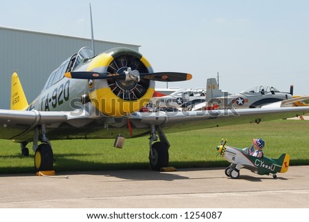 Little boy in a toy plane looking at an old WWII plane