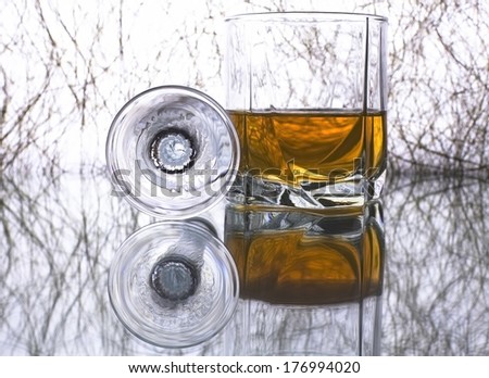 Tumbler of golden whiskey or brandy and empty glass on the original background  with reflection