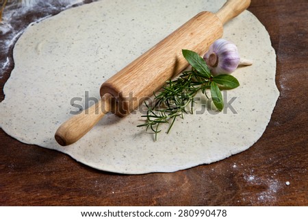 Wooden rolling pin with freshly prepared dough and dusting of flour on wooden background