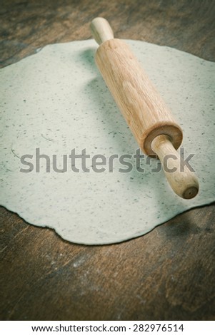 Wooden rolling pin with freshly prepared dough and dusting of flour on wooden background