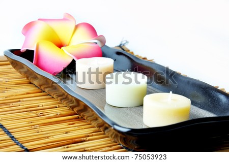 Three candles and plumeria in plate on bamboo mat