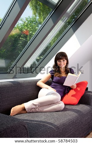 young woman laying on couch reading a book 6818