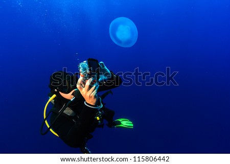 SCUBA Diver photographing a jellyfish in deep, blue open ocean
