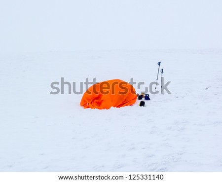 A bright orange snow survival shelter in a complete white out blizzard