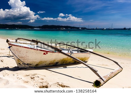 A traditional wooden outrigger style paddle boat sits on a tropical sandy beach
