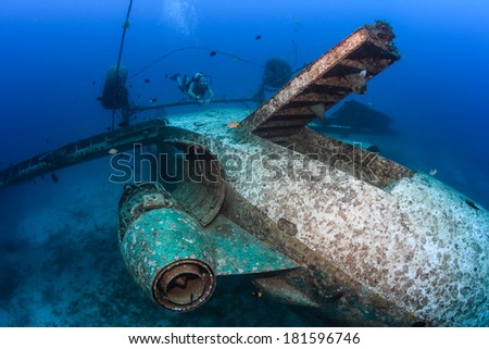 SCUBA diver above the upside down wreckage of an aircraft, deep underwater