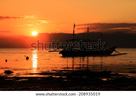 Tropical sunset with traditional boat silhouette on a calm ocean
