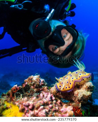 SCUBA diver examines a colorful Nudibranch on a tropical coral reef