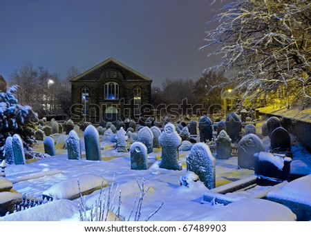 Church and graveyard covered in snow and lit by street lights