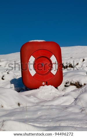 A red flotation life ring buried in snow near a frozen lake
