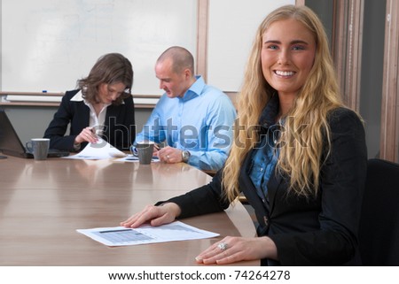 Young, stunning professional businesswoman smiling into the camera at an office board meeting
