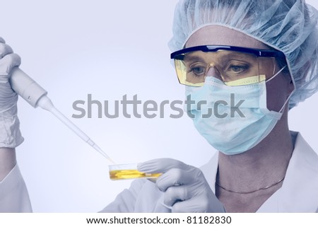Closeup of a female, caucasian lab technician with goggles and protective gear working with pipette and yellow liquid