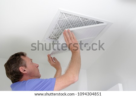 Man shutting grill of HVAC, heating ventilating and cooling after replacing the air filter. Closing ceiling grill after replacing an air filter in the ceiling.