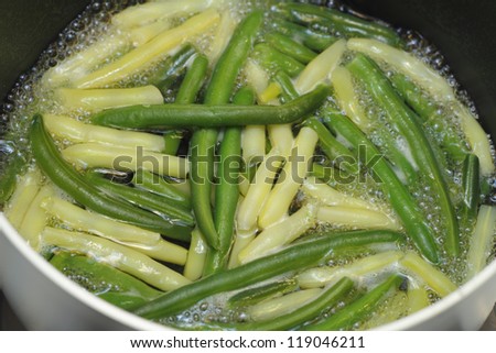 Boiling green and yellow wax beans in some water on the stove in a sauce pan.