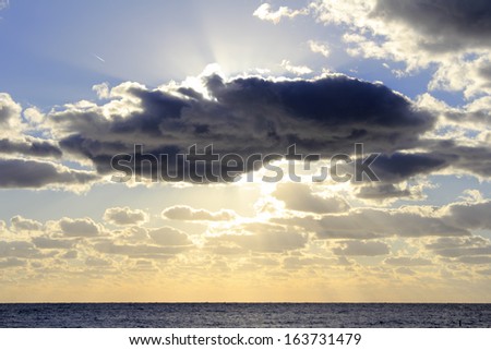 Beautiful sun streaming golden yellow white sunlight from behind a large blue cloud over the Atlantic Ocean off the coast of Lauderdale By The Sea one winter morning.