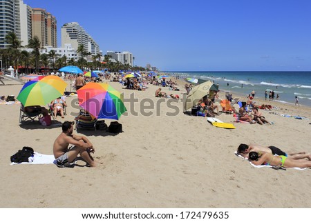 FORT LAUDERDALE, FLORIDA - APRIL 8, 2013: Colorful Atlantic coast beach scene of many people suntanning, relaxing and enjoying the shore during spring break on a hot and sunny, clear blue sky day.