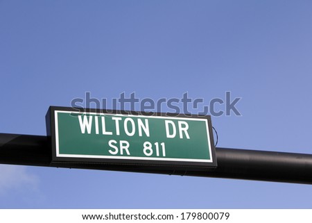 Green and white street sign over Wilton Drive also called State Route 811, seen in Wilton Manors, Florida on a sunny, blue sky day.