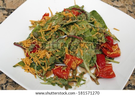 Salad of mixed baby greens, sweet red peppers, pumpkin seeds, cheddar cheese with balsamic vinegar and olive oil on a white plate.