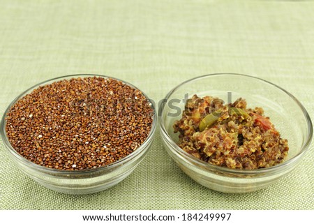 Uncooked red quinoa seeds in a round clear glass dish next to a tasty and healthy appetizer bowl of cooked quinoa mixed with jalapeno slices, tomatoes and parmesan cheese on a green place mat.