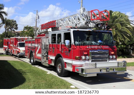 LIGHTHOUSE POINT, FLORIDA - FEBRUARY 12, 2014: One large, modern red fire engine truck with ladder and two red ambulances parked on a street responding to a call in a neighborhood on a sunny day.