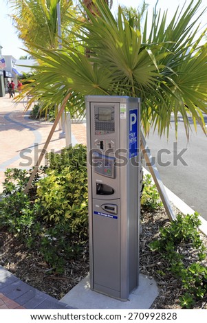 LAUDERDALE-BY-THE-SEA, FL, USA - APRIL 7, 2014: Closeup of an electric parking meter with signage in the shade of palm trees and plants of a newly redesigned parking lot.