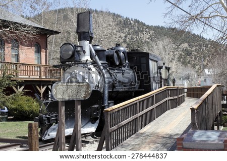 Idaho Springs, CO, USA - April 23, 2014: Front and side view of an old black train with historical information on a wood sign. A wooden walkway travels the length of the historical train