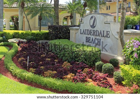 Fort Lauderdale, FL, USA - June 25, 2014: Large cement and metal Lauderdale Beach entrance sign with beautiful plants, trees, lawn and flowers around the sign. Lauderdale Beach entry sign