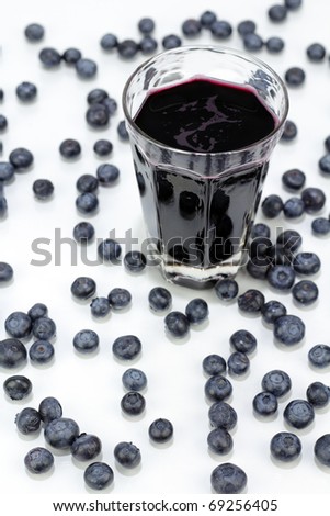 Deep purple berry juice in clear glass, whole fruit abstract on white reflective surface.
